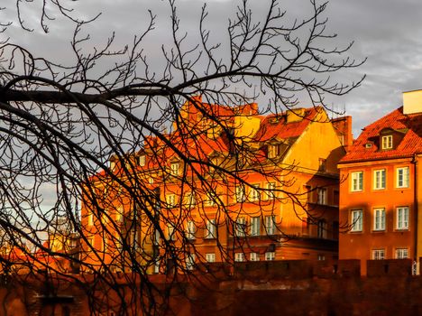 Historical buildings, the red brick walls of Warsaw Barbican, Poland and the silhouette of a tree branch in front of them at sunset in spring
