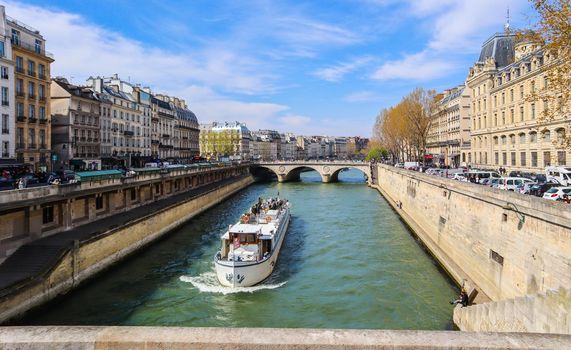 Paris / France - April 5, 2019: Beautiful cityscape of Paris, Saint-Michel bridge across Seine river and a tourist ship with tourists