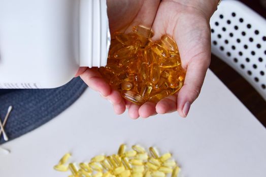 Omega-3 fish oil capsules are poured into hands from a large white jar. Medical healthcare, healthy food concept. Vitamin pills.