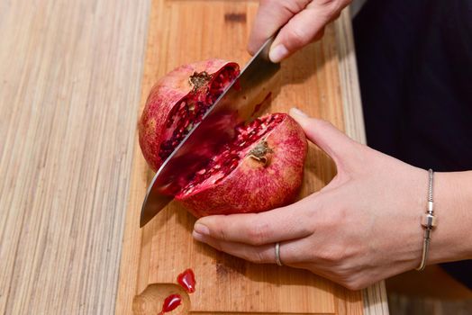 Female hands Cutting pomegranate in a kitchen. Close-up.