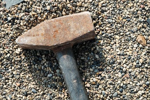 Close-up of large sledgehammer for crushing lies on small pebbles.