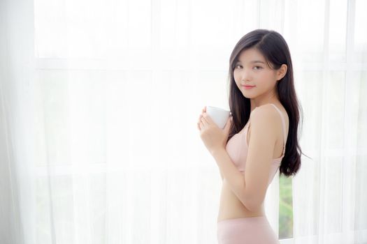 Beautiful young asian sexy woman in underwear drinking coffee near windows in the morning, girl with seductive figure fit drinking beverage for relax and resting after wake up, lifestyle concept.
