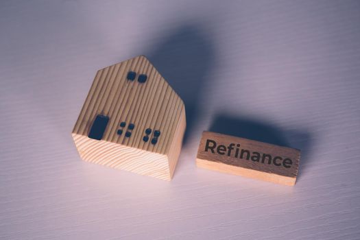 Wooden block with refinance word and house model about home and finance, loan and mortgage for real estate and property, residential and planning with budget, investment and earning, business concept.