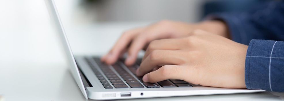 Employee young man typing and working on laptop computer on desk at home, business man using notebook and check email on table, hand of freelance is blogger, lifestyle concept, banner website.