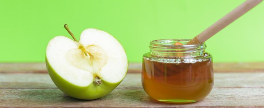 Jewish holiday, Apple Rosh Hashanah dessert, on the photo have honey in jar and green apples was sliced on wooden with green background