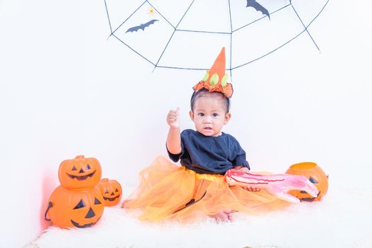Funny happy baby girl in Halloween costume with pumpkin Jack with Cobweb on background