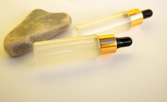 Two bottles of cosmetic liquid transparent gel next to a gray heart-shaped stone on a white background. Flat styling style