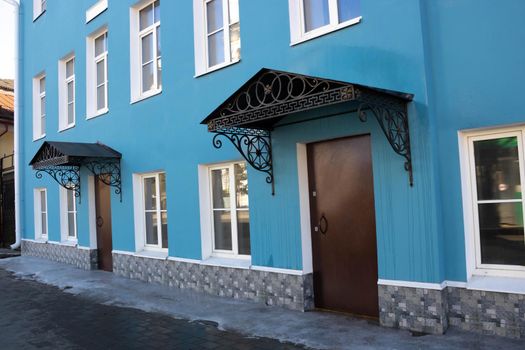 Side view of the blue facade with white windows, iron doors and wrought iron canopies.
