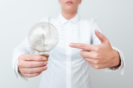 Lady Pointing To Lamp Held In Hand In Formal Outfit Presenting New Ideas For Project, Business Woman Carying Bulb Exhibiting Lately Released Technologies, Lightbulb Veiwing Fresh Idea.