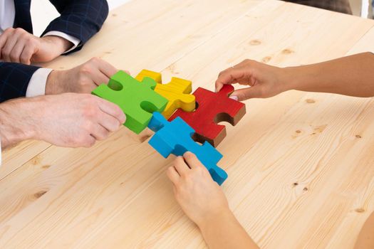 Multi-ethnic group of people assembling jigsaw puzzle together, hands joining pieces at desk, successful teamwork concept, team building activity, help and support in business, close up view