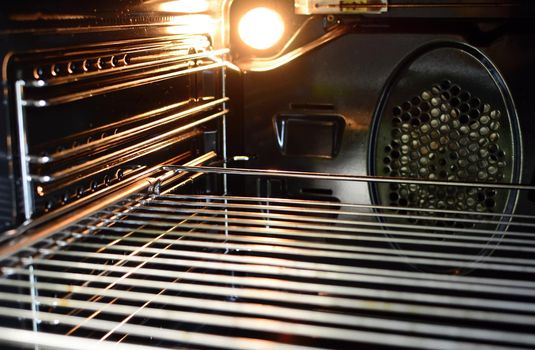 A view of the inside of an empty oven with lighting bulb and a wire rack.