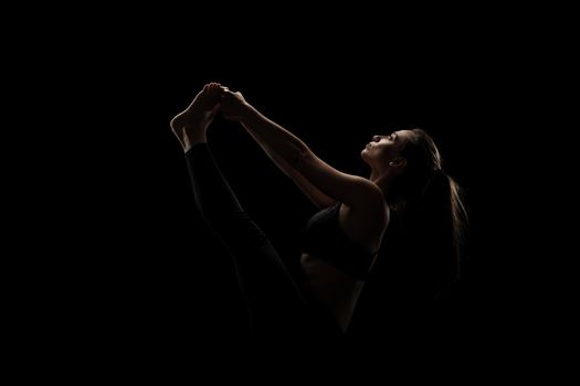 cute caucasian girl exercising yoga poses against dark backgroung. side lit silhouette.