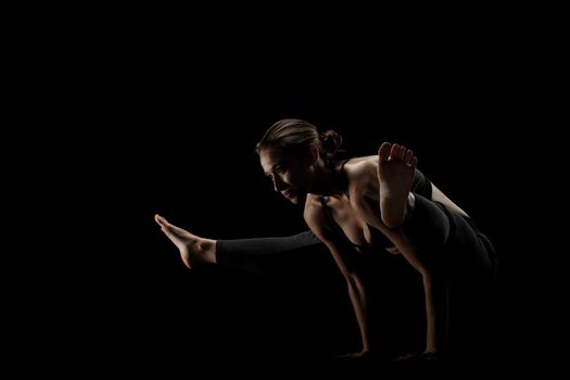 cute caucasian girl exercising yoga poses against dark backgroung. side lit silhouette.