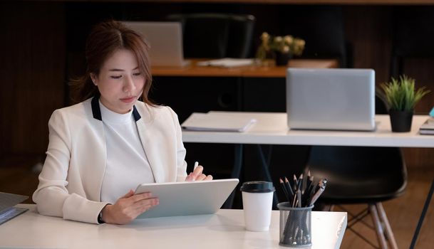 Young asian female in business suit using on digital tablet at her office, Woman working for business financial