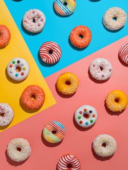 Assorted colorful glazed donuts, top view. Creative layout made from delicious glazed donuts. Vertical flat lay background with multicolored donuts or doughnuts. Blue yellow pink backdrop. Hard light