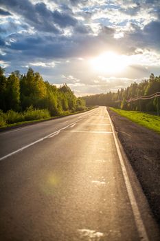 Country road with markings in the middle of the forest. Path and forward movement in the sun. Beautiful, green forest in the spring at sunset. Concept for success in the future goal and passing time