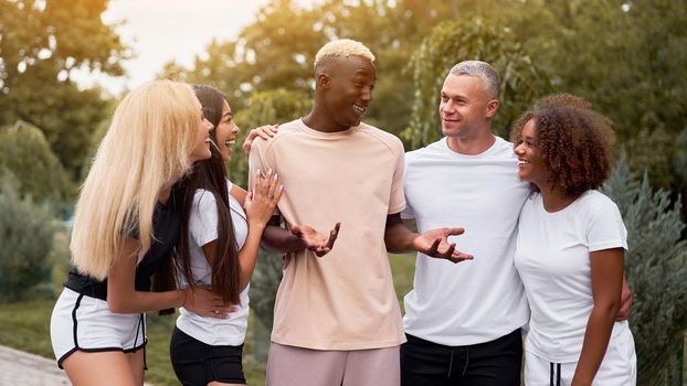 Multi-ethnic group teenage friends. African-american asian caucasian student spending time together Multiracial friendship Happy smiling People dressed black white sportswear meeting outdoor