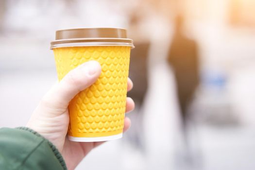 unrecognizable man holding yellow paper cup with coffee in hand on blured street background