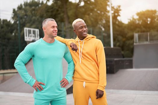 Multi-ethnic friendship Black african-american and caucasian guy friends spending time together on skate park Two multi ethnic student Dressed colorful sportswear.