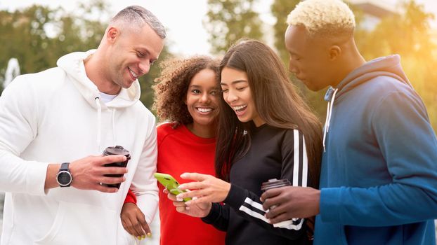 Multi-ethnic group teenage friends looking smartphone screen. African-american asian caucasian student spending time together Multiracial friendship Smiling People colorful sportswear drink coffee