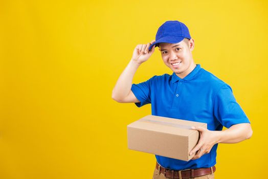 Portrait excited attractive delivery happy man logistic standing he smile wearing blue t-shirt and cap uniform holding parcel box looking to camera, studio shot isolated on yellow background