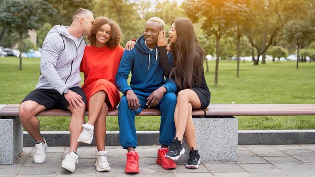 Multi-ethnic group teenage friends. African-american asian caucasian student spending time together Multiracial friendship Happy smiling People dressed colorful sportswear sitting bench park outdoor