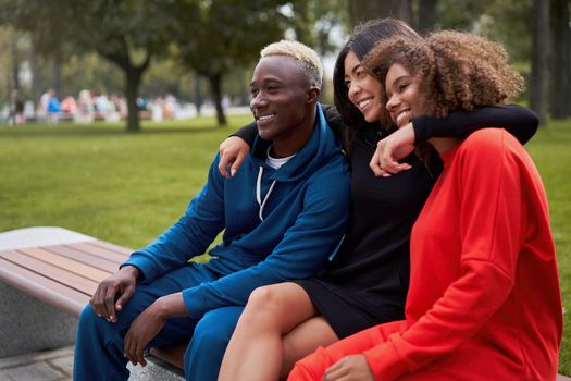 Multi-ethnic group teenage friends. African-american asian student spending time together Multiracial friendship Happy smiling People dressed colorful sportswear sitting bench park outdoor