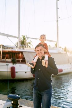 Little girl is sitting on her daddy's shoulders on a boat pier in Porto Montenegro. High quality photo