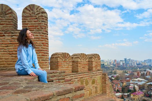 The girl enjoys the view and the silence while sitting on the wall of an ancient fortress overlooking the city.