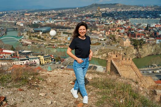 A cute brunette girl enjoys the stunning scenery of Tbilisi from the hill. The whole city at her feet.