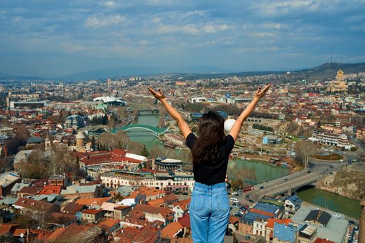 A cute brunette girl enjoys the stunning scenery of Tbilisi from the hill. The whole city at her feet.