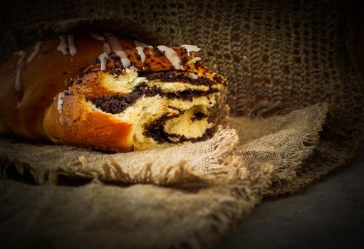 Fresh poppy seed roll on natural linen napkin on rustic wooden background