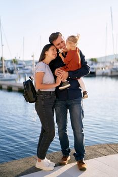 Beautiful family is hugging each other and enjoying a sunny day on a boat pier by the sea. High quality photo