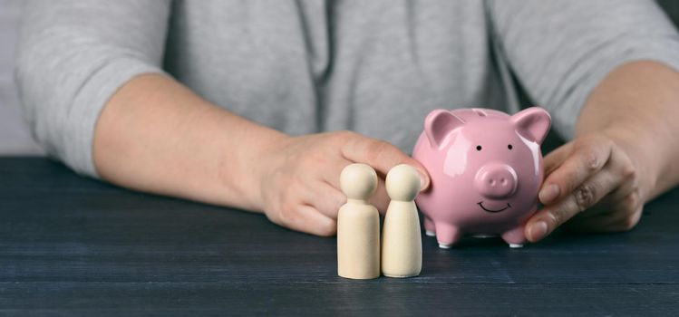 wooden figurines of little men family on the background of a man with a piggy bank. The concept of savings and long-term budgeting, cost savings. Cash back from purchases, benefit