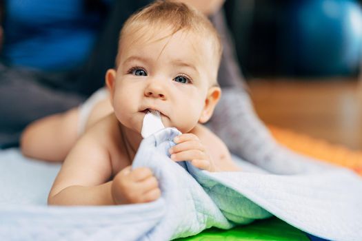 Tiny baby in diapers lies with his tummy on a blue blanket and holds the edge with his hands and teeth. High quality photo