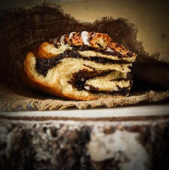 Fresh poppy seed roll on natural linen napkin on rustic wooden background