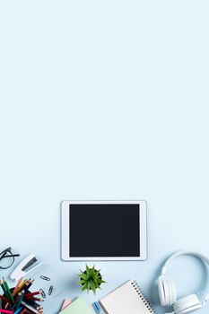 Online learning design concept. Top view of student table with tablet, headphone and stationeries on blue table background.