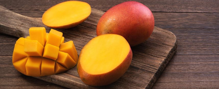 Mango. Close up of fresh ripe mango fruit with leaves over dark wooden table background with green leaves.