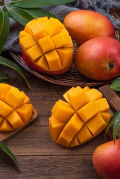 Mango. Close up of fresh ripe mango fruit with leaves over dark wooden table background with green leaves.