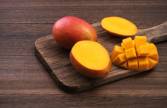 Mango. Close up of fresh ripe mango fruit with leaves over dark wooden table background with green leaves.