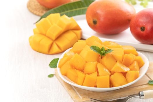 Diced fresh mango fruit on a white plate with leaves over wooden table background.