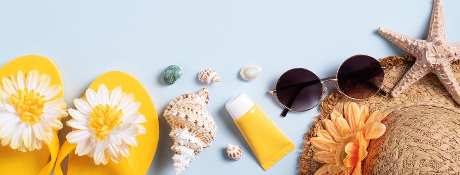 Summer beach background design concept. Top view of holiday travel with shells, hat, slipper on blue background.