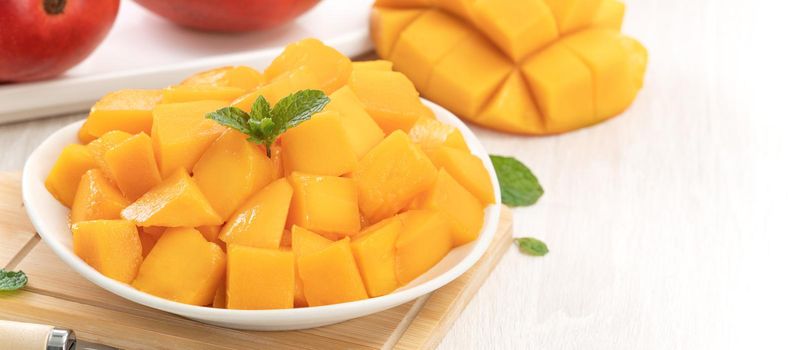 Diced fresh mango fruit on a white plate with leaves over wooden table background.