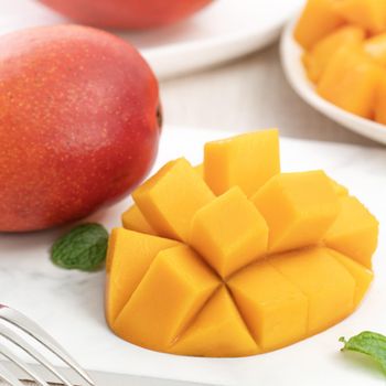 Diced fresh mango fruit on a white plate with leaves over wooden table background.
