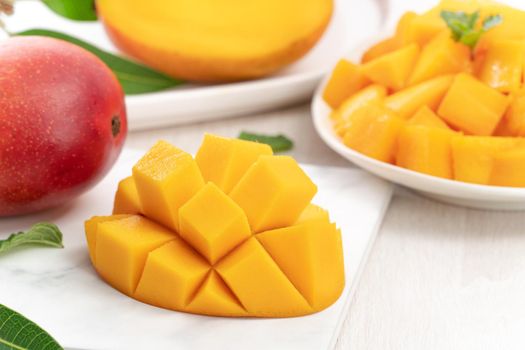 Diced fresh mango fruit on a white plate with leaves over wooden table background.
