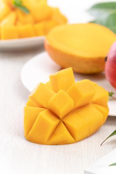 Diced fresh mango fruit on a white plate with leaves over wooden table background.
