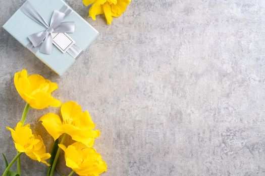 Mother's day background concept. Top view design of holiday greeting gift with yellow tulip bouquet on bright gray table background