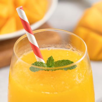 Fresh beautiful delicious mango juice. Close up design concept of smoothie cold drink in a glass cup with paper straw on gray table background.