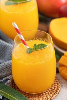 Fresh beautiful delicious mango juice. Close up design concept of smoothie cold drink in a glass cup with paper straw on gray table background.