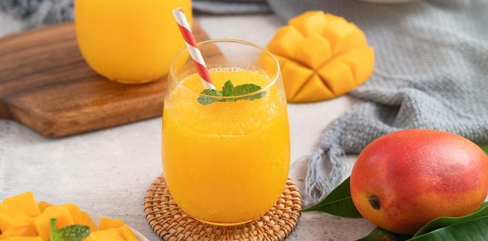 Fresh beautiful delicious mango juice. Close up design concept of smoothie cold drink in a glass cup with paper straw on gray table background.
